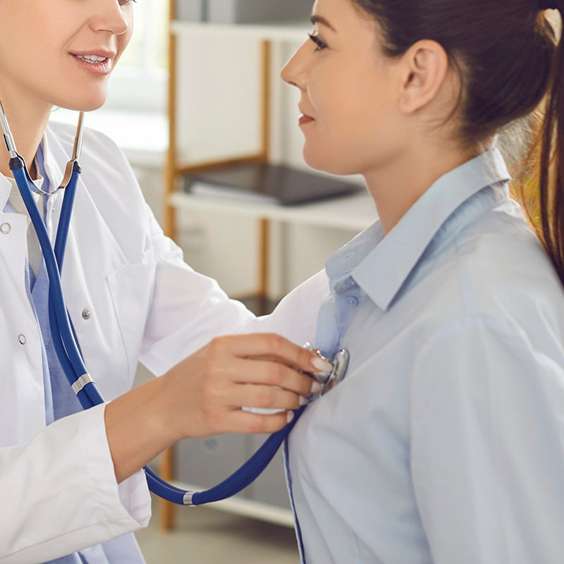 Eine jüngere Frau wird mit einem Stethoscope am Herzen abgehört.