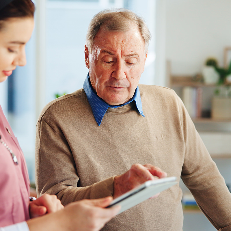 Ein älterer Mann zeigt auf Untersuchungsunterlagen einer Arzthelferin einen Punkt. Er zeigt darauf.