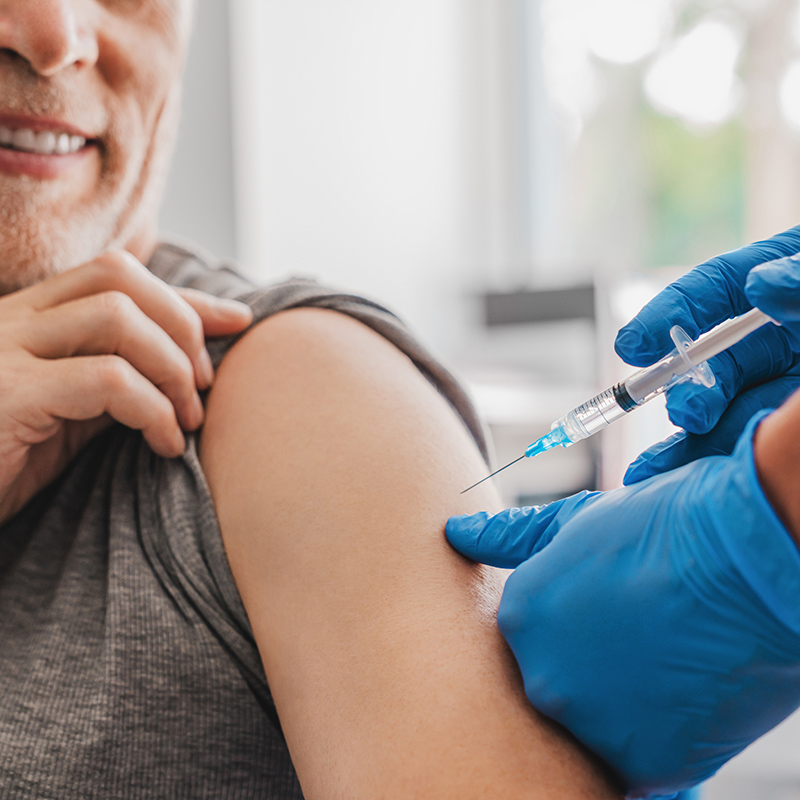 Ein Mann mittleren Alters bekommt eine Spritze in den linken Oberarm.