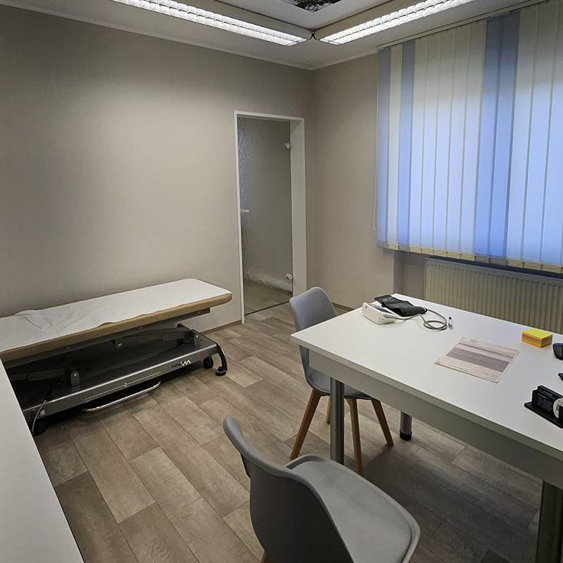 Behandlungsraum mit Tisch und Stühlen und einer Liege in heller Raumbeleuchtung