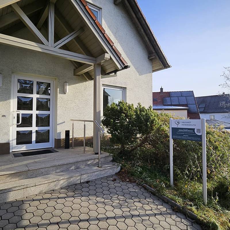 Aussenansicht des Eingangs der Hausarztpraxis mit Firmenschild seitlich