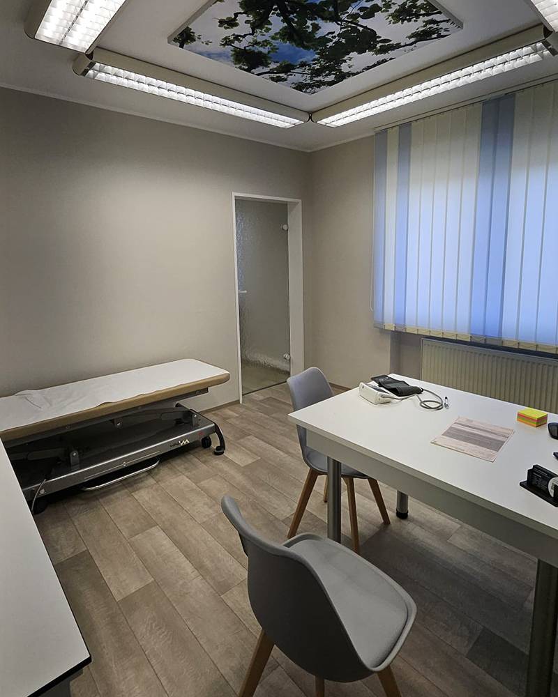 Behandlungsraum mit Tisch und Stühlen und einer Liege in heller Raumbeleuchtung