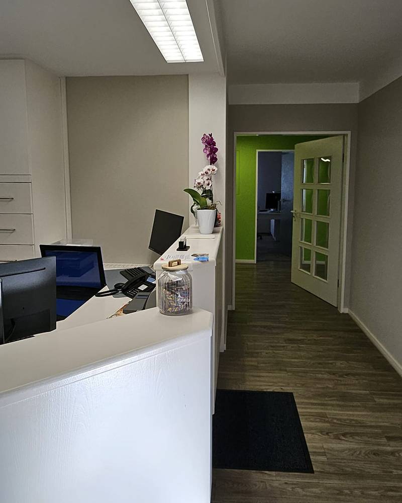 Eingangsbereich mit Begrüßungstheke. Ein Gang führt zu Behandlungszimmern.